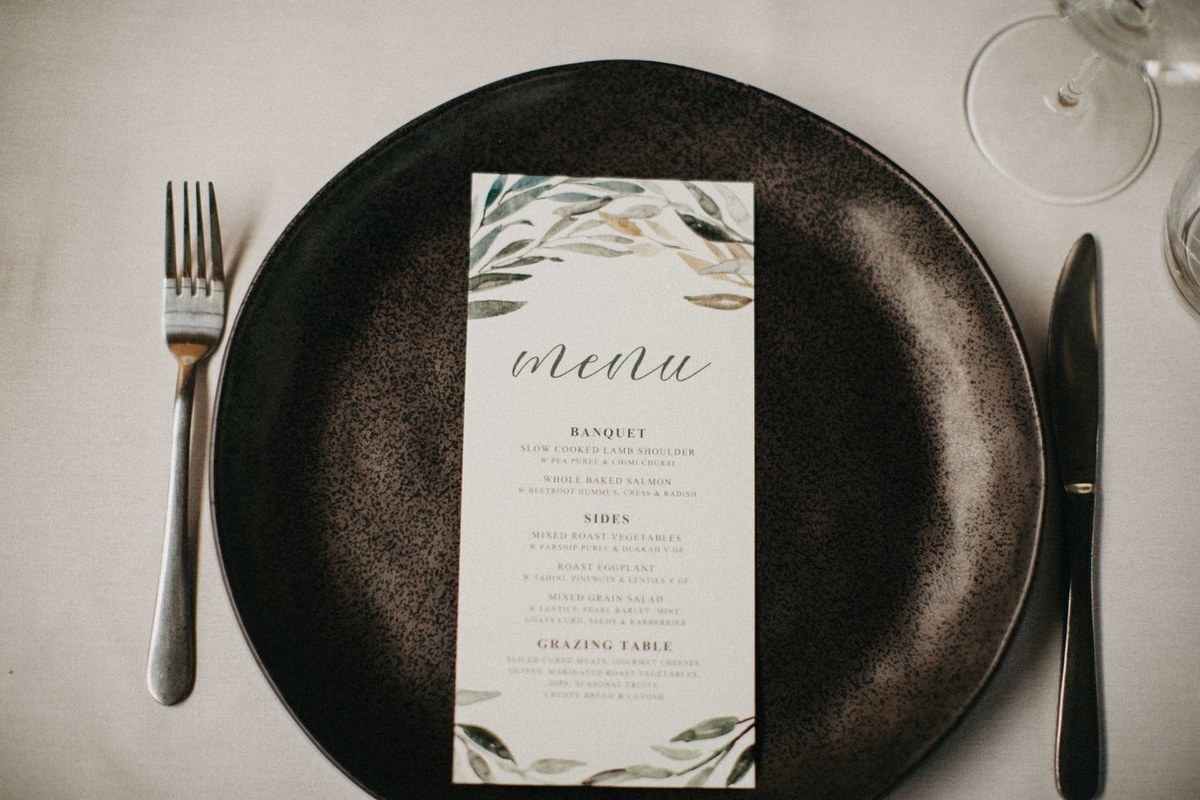 Wedding menu at Redleaf Wollombi — Joshua Mikhaiel, documentary wedding photographer A printed menu is centered on a dark plate beside cutlery. Photograph by documentary wedding photographer Joshua Mikhaiel.