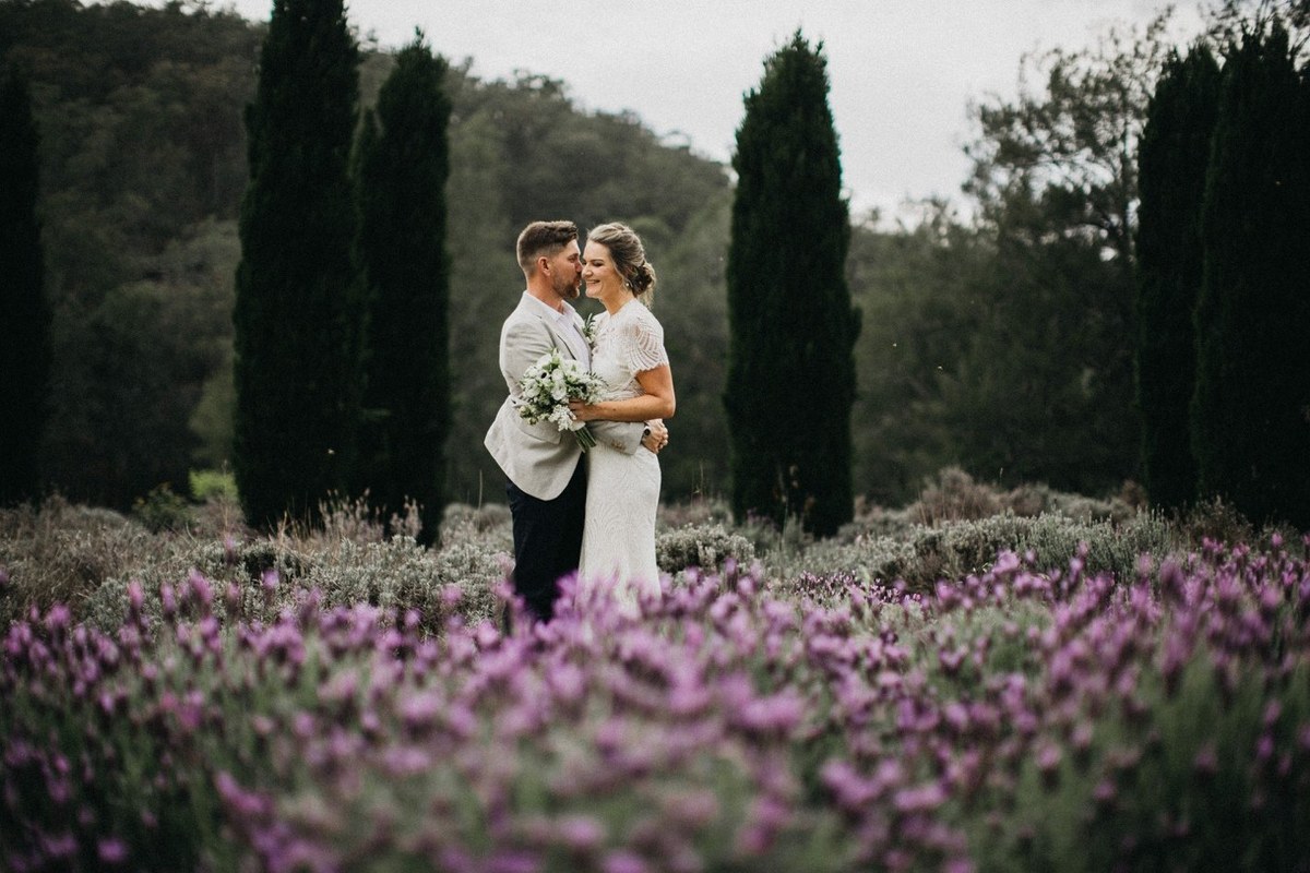 Couple portrait at Redleaf Wollombi — Joshua Mikhaiel, documentary wedding photographer The bride and groom pose among a bed of purple flowers and tall trees. Photograph by documentary wedding photographer Joshua Mikhaiel.