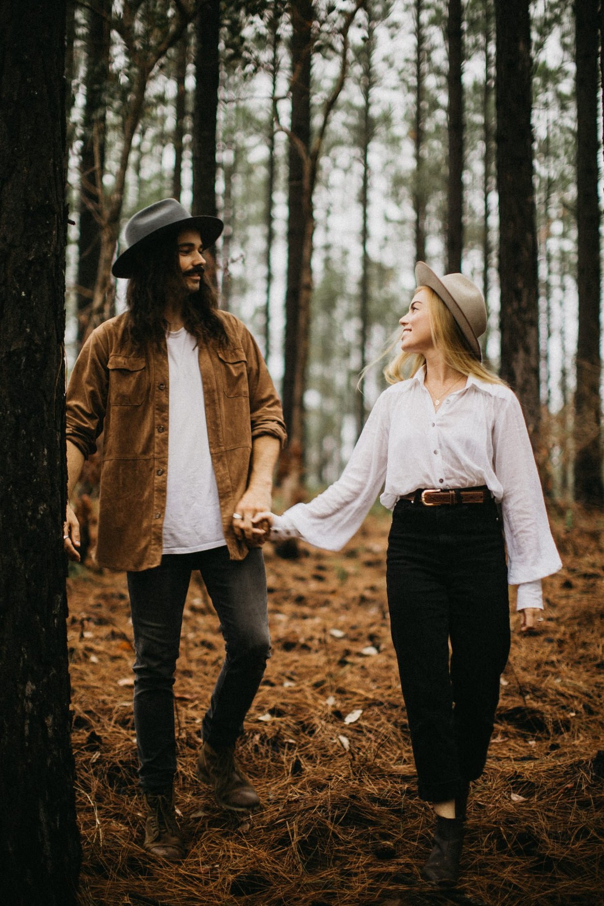 Woodland engagement portrait — Joshua Mikhaiel, documentary wedding photographer A couple hold hands between tall trees during an engagement session photographed by documentary wedding photographer Joshua Mikhaiel.