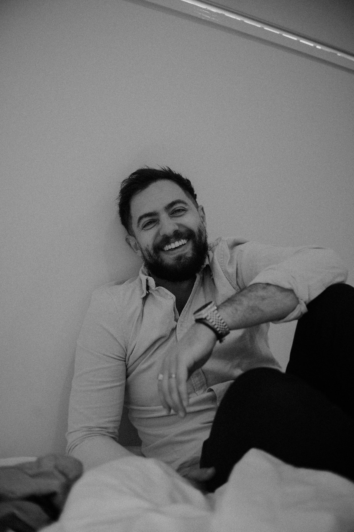 Portrait of Joshua Mikhaiel, documentary wedding photographer Documentary wedding photographer Joshua Mikhaiel sits smiling in a relaxed portrait.
