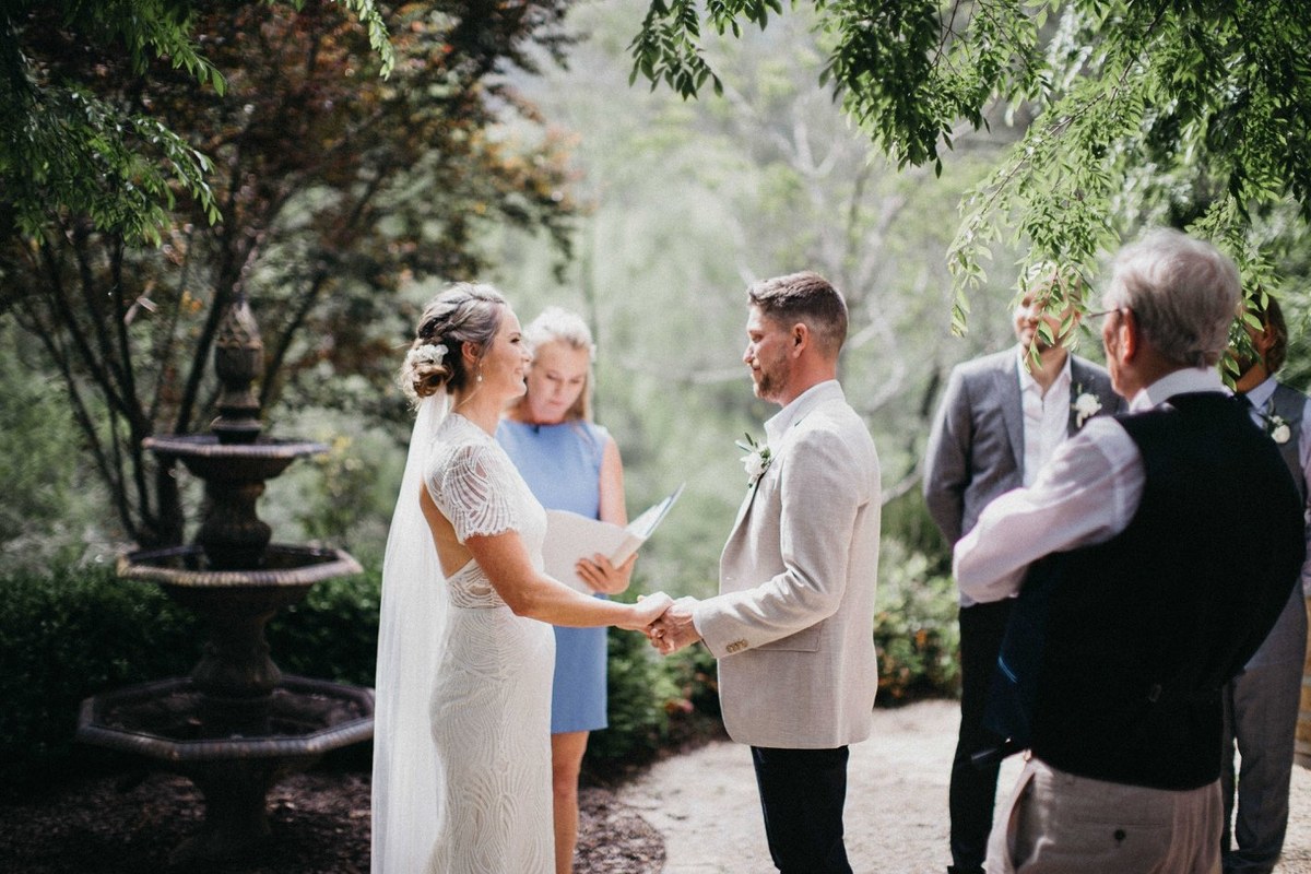 Bride with a guest at Redleaf Wollombi — Joshua Mikhaiel, documentary wedding photographer The bride holds hands with an older man beneath the garden trees. Photograph by documentary wedding photographer Joshua Mikhaiel.